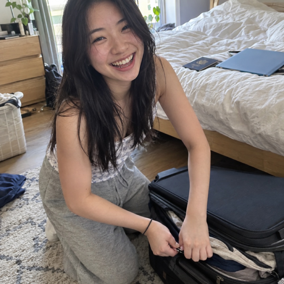 A student zipping up a packed suitcase at home